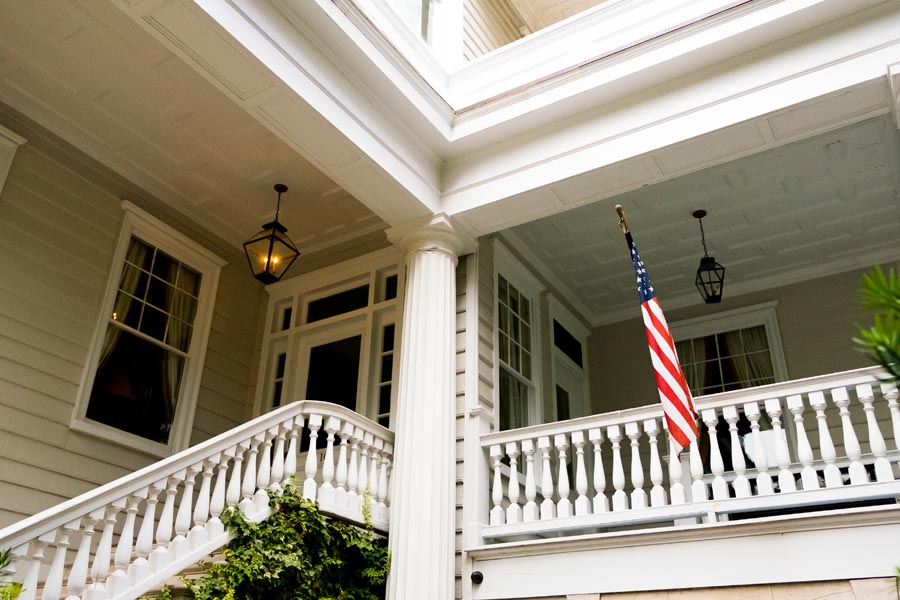 About Our Agency - Front Porch of a Home With an American Flag Hanging Outside